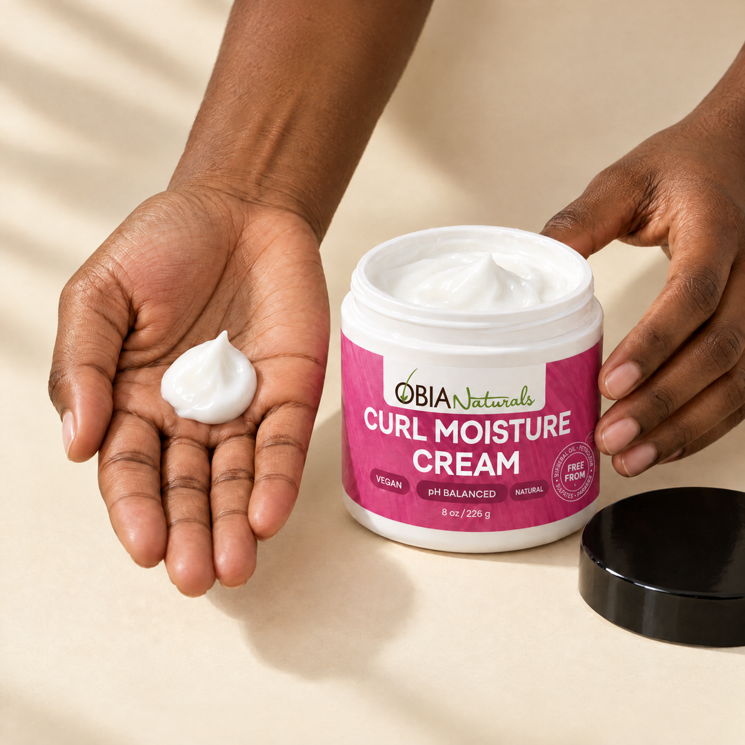 A quarter-sized amount of OBIA Curl Moisture Cream in the palm, next to the open jar